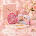 Two small bags, one pink with a girl design and the other multicolored with a bear design, on a pink surface with flowers and cards.