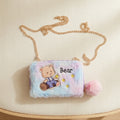 Fluffy children's bag with teddy bear design and gold chain on a beige surface