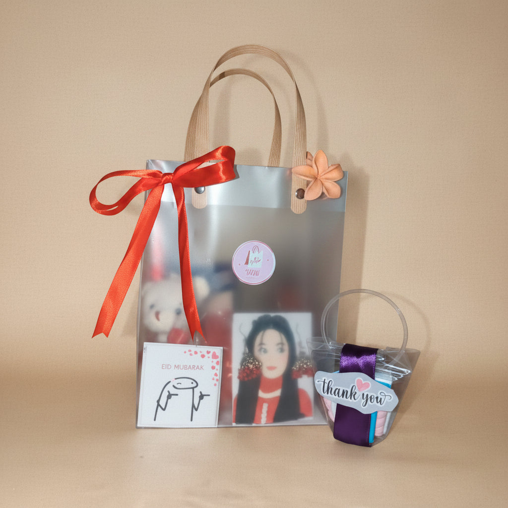 Gift bag with a red ribbon, small figurines, and a card on a wooden surface.
